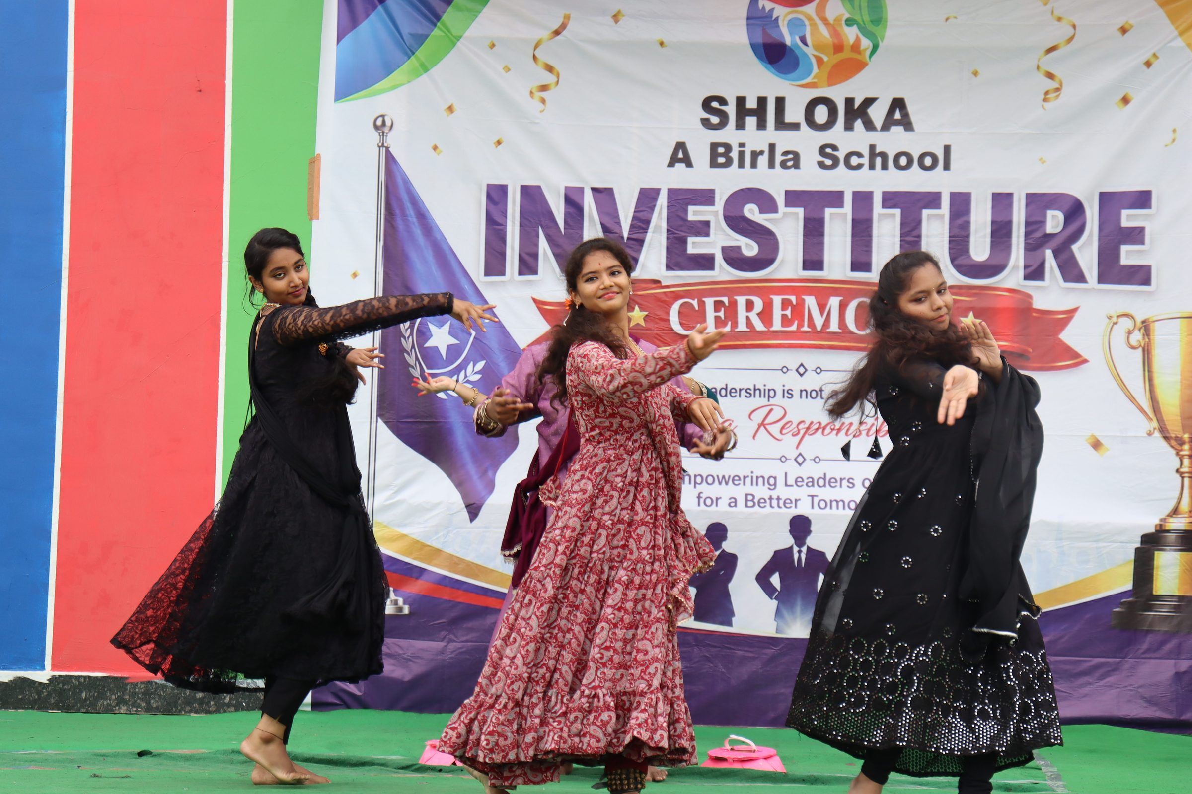Three students in traditional dress performing a cultural dance on the investiture ceremony stage