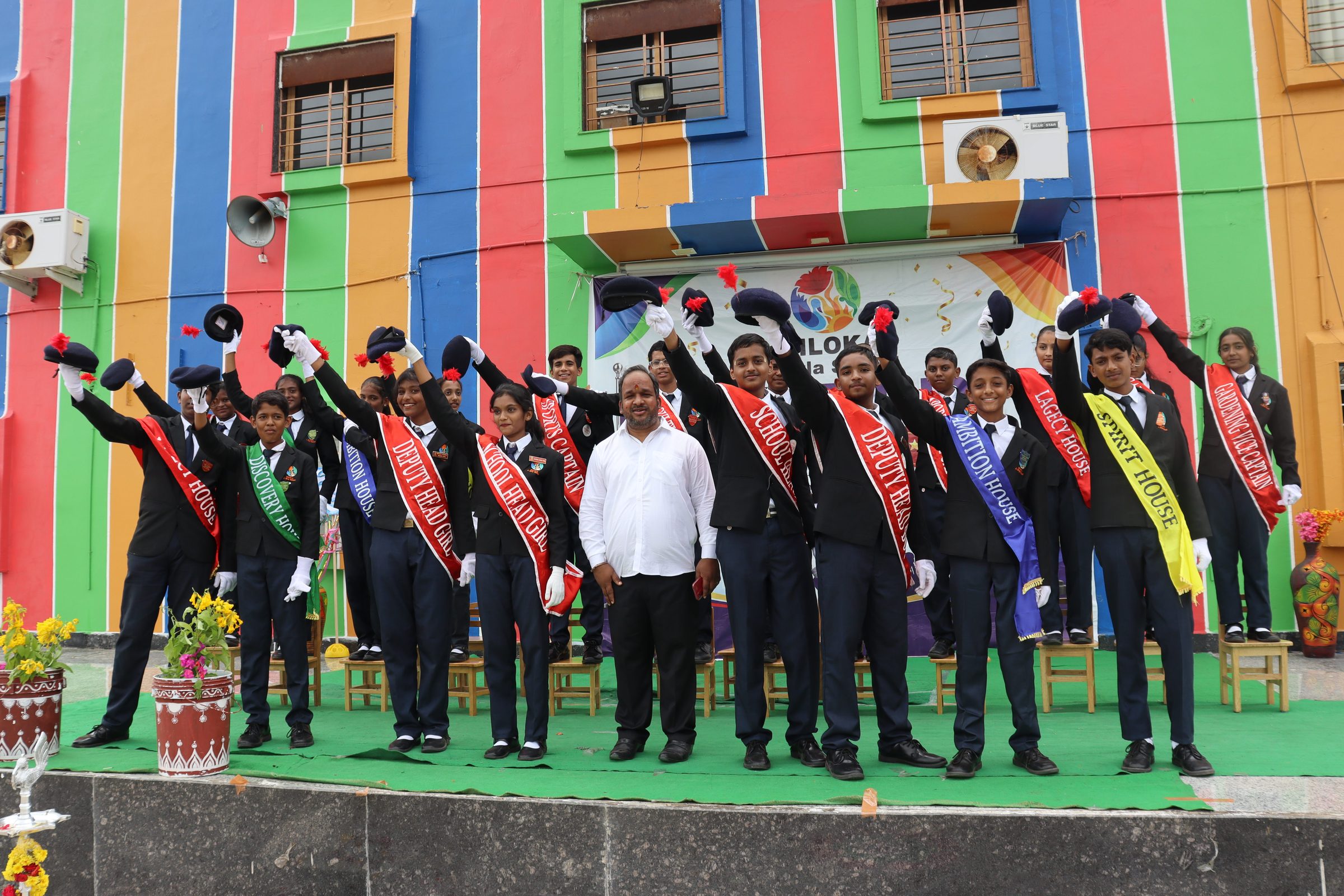 The newly appointed student council standing on stage with hands raised, taking the oath of office at the SHLOKA - A Birla School investiture ceremony